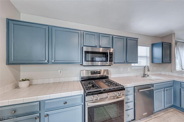 kitchen featuring light tile patterned floors, tile counters, stainless steel appliances, blue cabinetry, and a sink