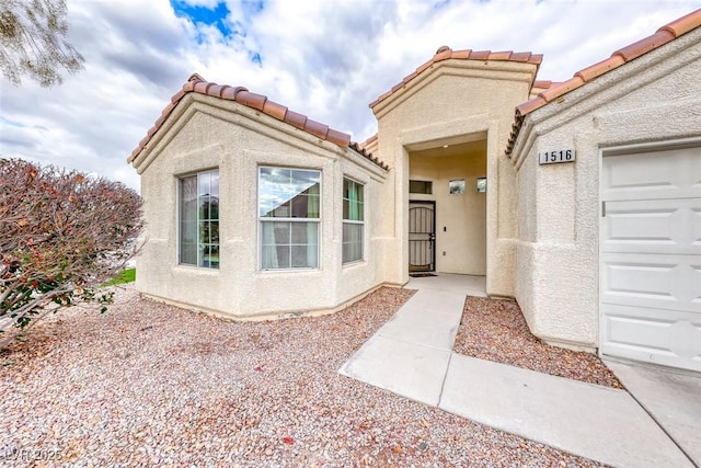 property entrance with an attached garage, a tile roof, and stucco siding