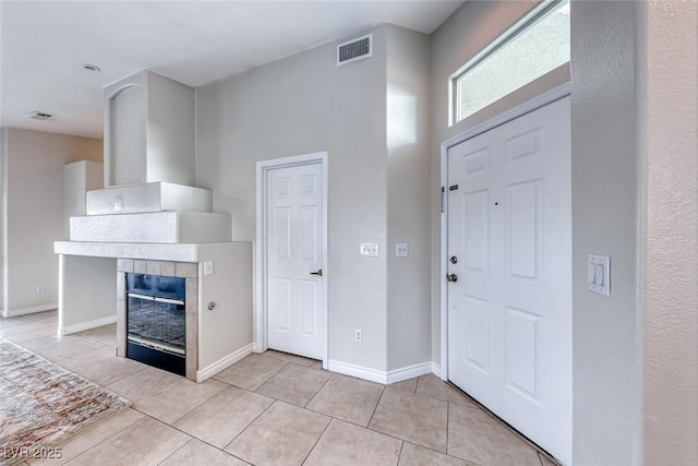 foyer with light tile patterned floors, a tile fireplace, visible vents, and baseboards