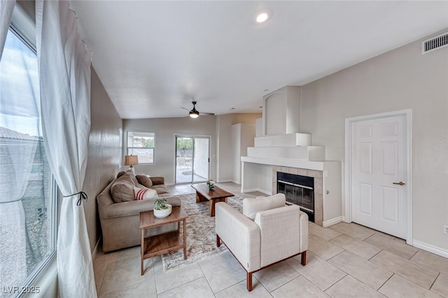 living area featuring light tile patterned floors, baseboards, visible vents, a ceiling fan, and a tile fireplace