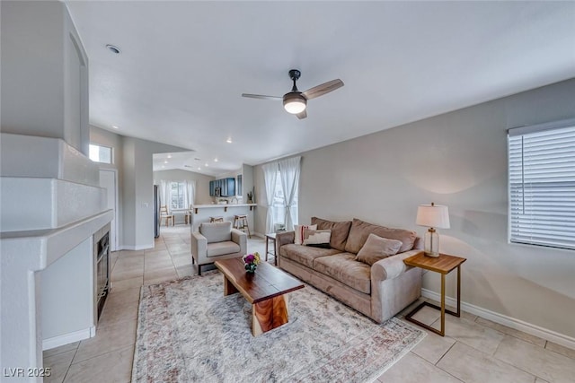 living room featuring vaulted ceiling, light tile patterned floors, a tile fireplace, and baseboards