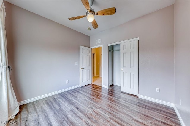 unfurnished bedroom featuring ceiling fan, wood finished floors, visible vents, baseboards, and a closet