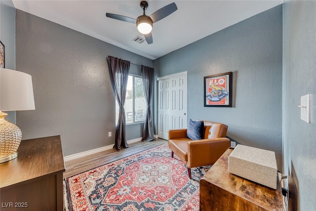 living area featuring visible vents, a textured wall, ceiling fan, wood finished floors, and baseboards