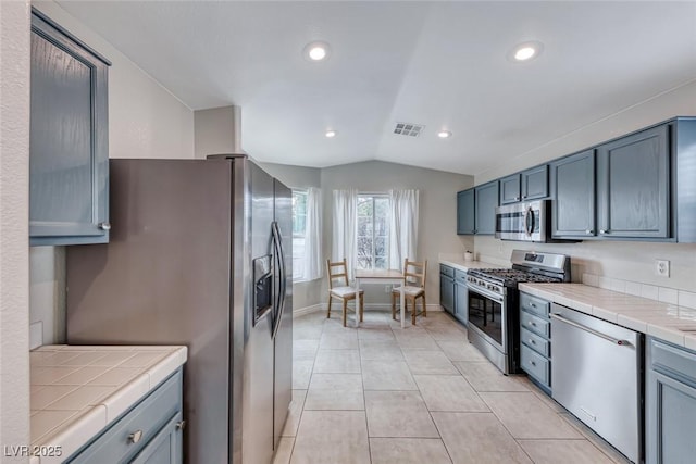 kitchen featuring light tile patterned floors, lofted ceiling, stainless steel appliances, visible vents, and tile counters