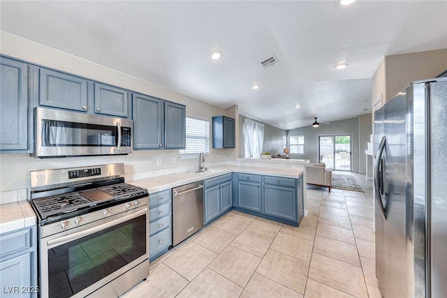 kitchen featuring stainless steel appliances, a peninsula, a sink, open floor plan, and light countertops