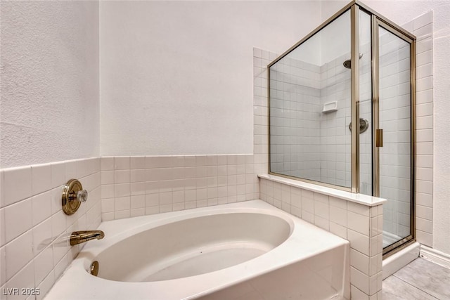 bathroom with a stall shower, tile patterned floors, a bath, and a textured wall