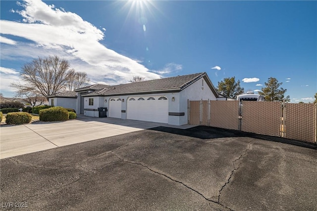 view of front facade featuring stucco siding, concrete driveway, an attached garage, a gate, and fence