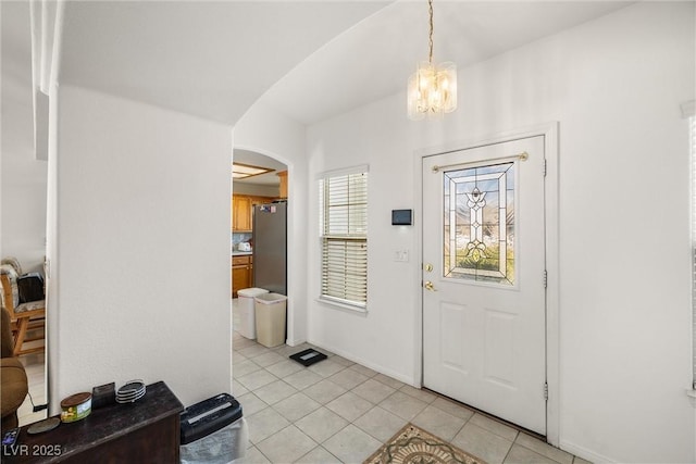 entrance foyer with arched walkways, light tile patterned floors, a chandelier, and baseboards