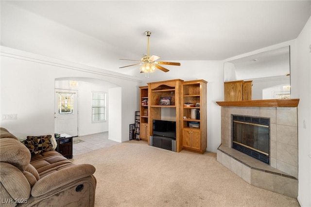 living room with light carpet, a fireplace, arched walkways, and a ceiling fan