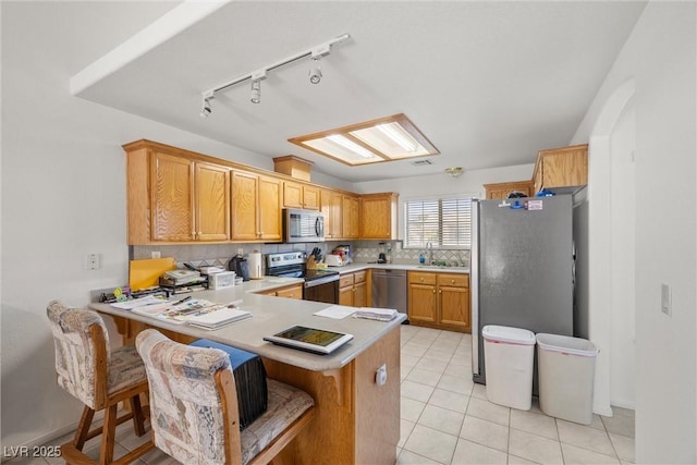 kitchen with light countertops, backsplash, appliances with stainless steel finishes, light tile patterned flooring, and a peninsula