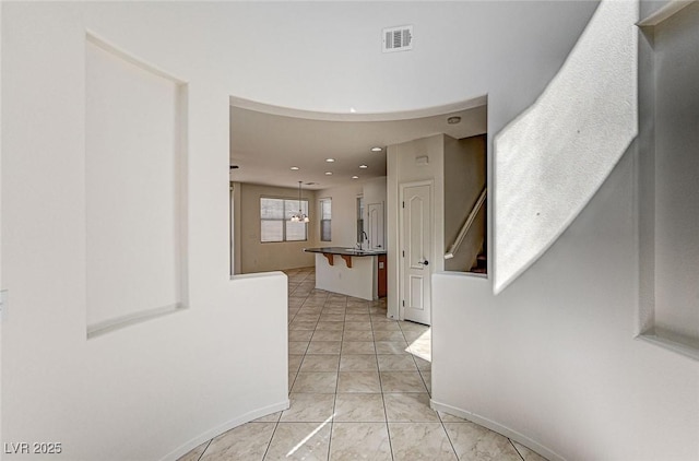 corridor with light tile patterned flooring, recessed lighting, a sink, visible vents, and baseboards