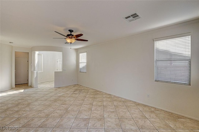 empty room with light tile patterned floors, visible vents, arched walkways, baseboards, and ceiling fan