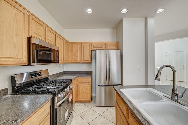 kitchen featuring dark countertops, stainless steel appliances, light brown cabinets, a sink, and recessed lighting