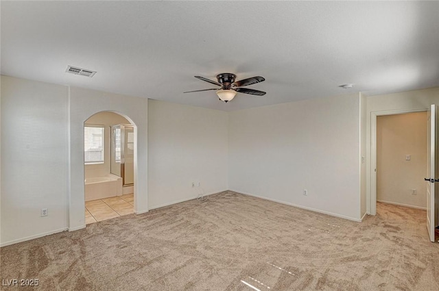 carpeted empty room with arched walkways, visible vents, ceiling fan, and baseboards