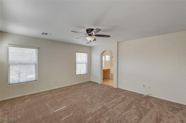 carpeted empty room featuring baseboards, visible vents, arched walkways, and a ceiling fan