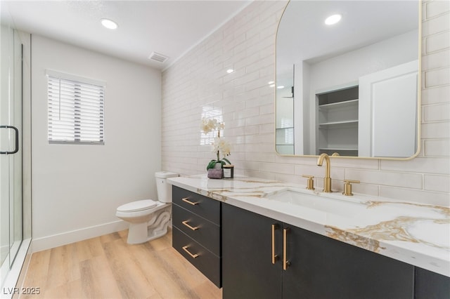 bathroom with toilet, wood finished floors, vanity, visible vents, and decorative backsplash