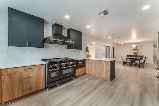 kitchen with range with two ovens, visible vents, wall chimney range hood, modern cabinets, and a peninsula