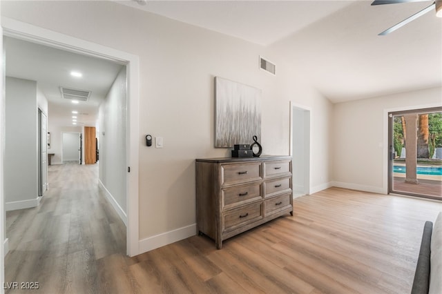 corridor featuring light wood-style flooring, visible vents, vaulted ceiling, and baseboards