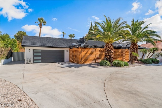 view of front of property featuring driveway, an attached garage, fence, roof mounted solar panels, and stucco siding