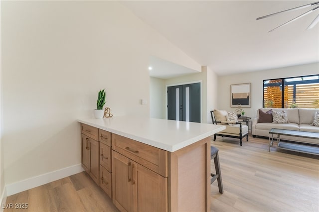 kitchen with baseboards, open floor plan, a peninsula, light wood-style floors, and a kitchen bar