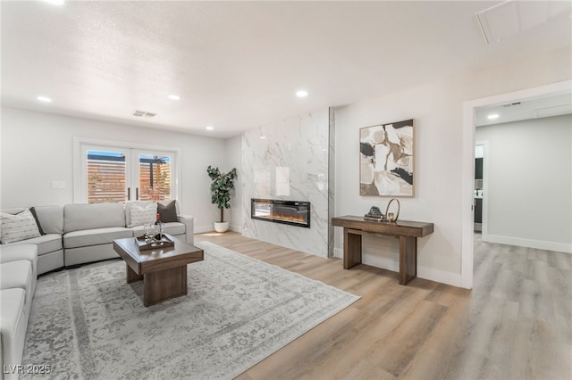 living room with recessed lighting, visible vents, wood finished floors, and a high end fireplace