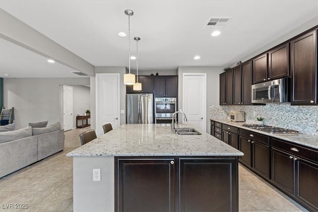 kitchen with dark brown cabinetry, stainless steel appliances, a sink, open floor plan, and tasteful backsplash