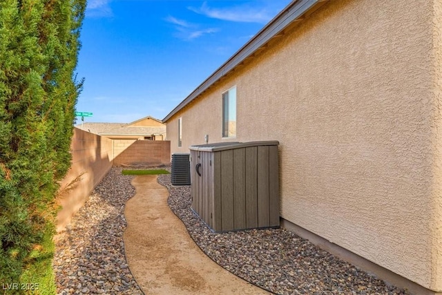 view of side of home with central AC, fence, and stucco siding