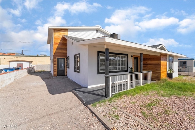 view of front of property featuring covered porch, roof with shingles, fence, and stucco siding