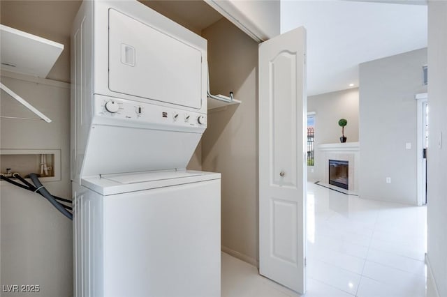 clothes washing area featuring laundry area, a tiled fireplace, stacked washer / drying machine, and light tile patterned flooring