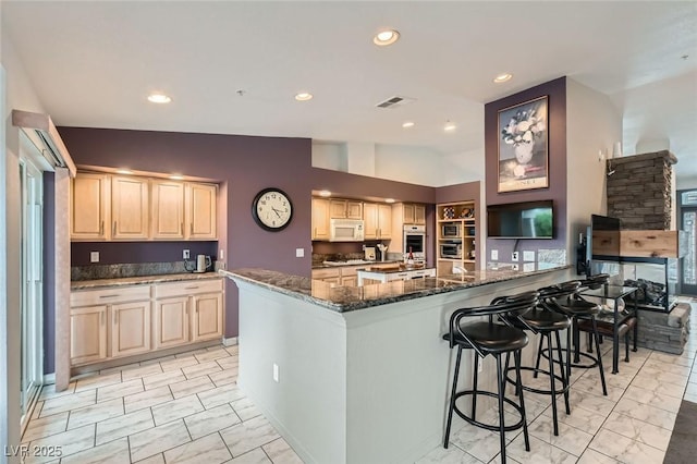 kitchen featuring dark stone counters, white appliances, visible vents, and light brown cabinetry