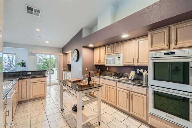 kitchen with white appliances, visible vents, vaulted ceiling, light brown cabinetry, and dark stone countertops