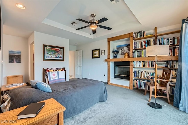 carpeted bedroom featuring a tray ceiling, visible vents, and a fireplace