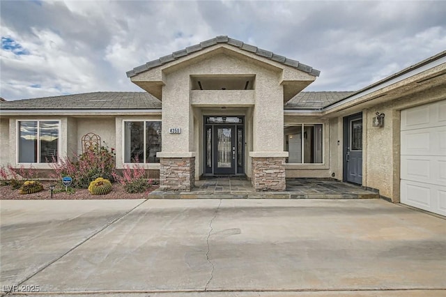 view of exterior entry featuring a garage, stone siding, and stucco siding