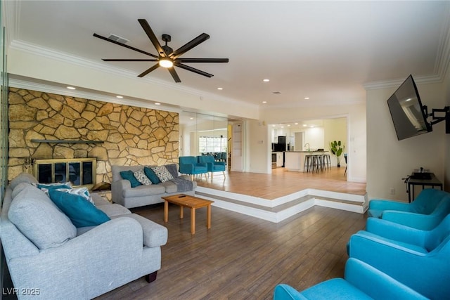 living room with recessed lighting, visible vents, ornamental molding, a stone fireplace, and wood finished floors