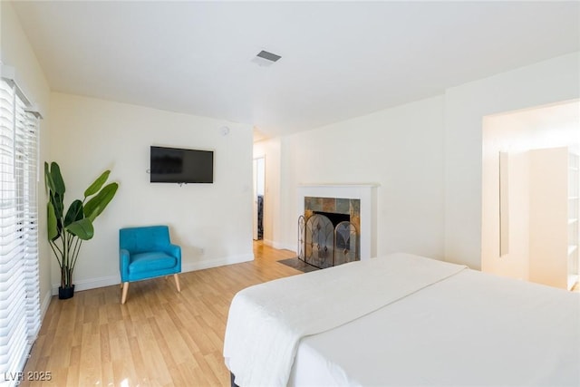 bedroom with light wood-style flooring, visible vents, baseboards, and a tile fireplace