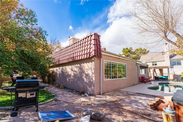 view of property exterior featuring an outdoor pool, a patio area, a tile roof, and stucco siding