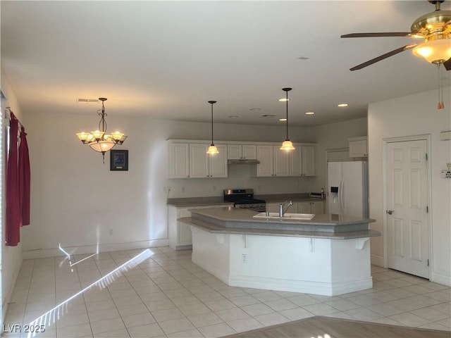 kitchen with visible vents, stainless steel gas range, a kitchen island with sink, a sink, and white refrigerator with ice dispenser