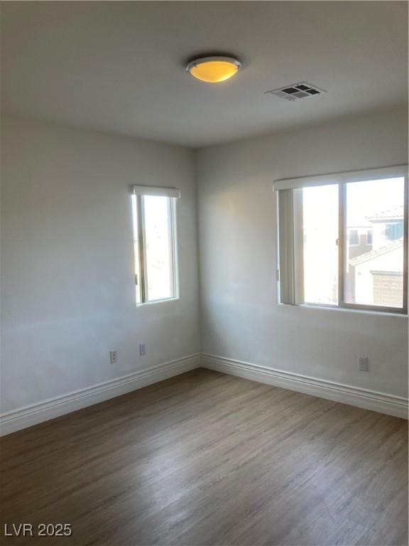 unfurnished room with wood finished floors, baseboards, and visible vents