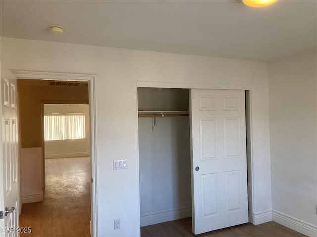 unfurnished bedroom featuring a closet, baseboards, visible vents, and wood finished floors