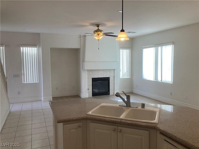 kitchen with a ceiling fan, a sink, open floor plan, light tile patterned floors, and a tile fireplace