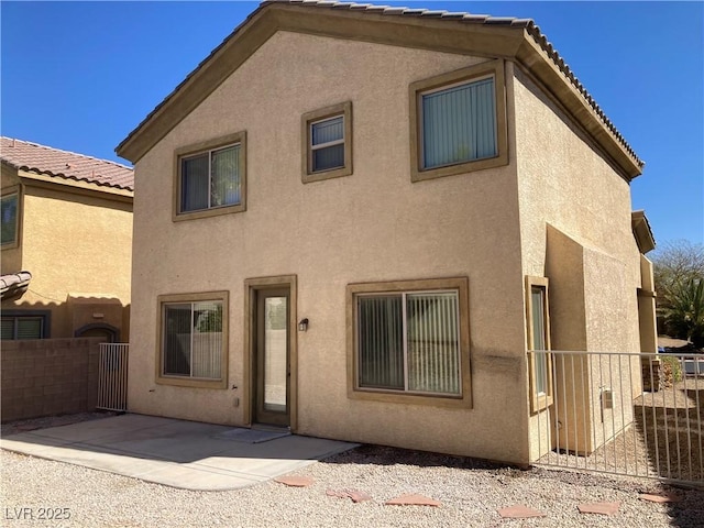 rear view of property with stucco siding, a tile roof, a patio, and fence