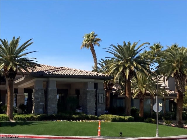 view of front of property featuring a front yard, a tiled roof, stone siding, and stucco siding