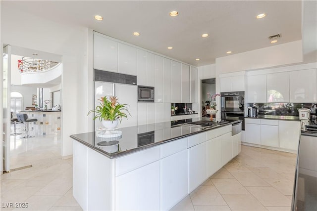 kitchen with white cabinets, dark countertops, a large island, modern cabinets, and black appliances