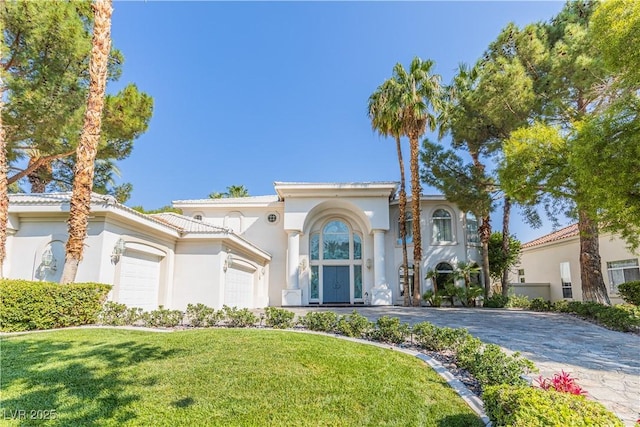 mediterranean / spanish house featuring decorative driveway, a tile roof, stucco siding, a garage, and a front lawn