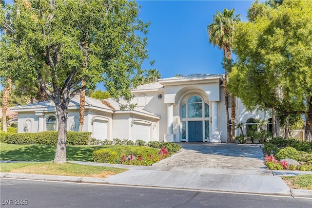 mediterranean / spanish house with a tiled roof, a front lawn, decorative driveway, and stucco siding