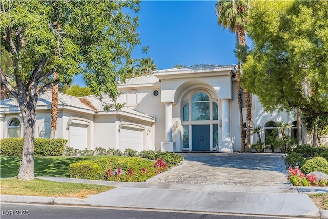 mediterranean / spanish home featuring a garage, decorative driveway, a tiled roof, and stucco siding