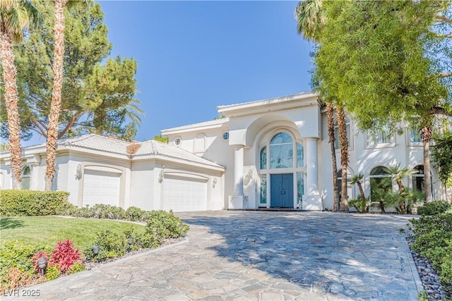 mediterranean / spanish-style home featuring a garage, decorative driveway, a tile roof, and stucco siding