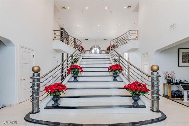 staircase with arched walkways, visible vents, a high ceiling, and tile patterned floors