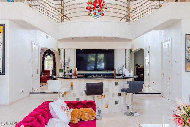 living area with a towering ceiling, light tile patterned floors, and arched walkways