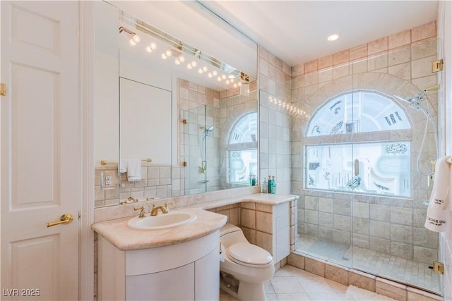 bathroom featuring a stall shower, vanity, toilet, and tile walls